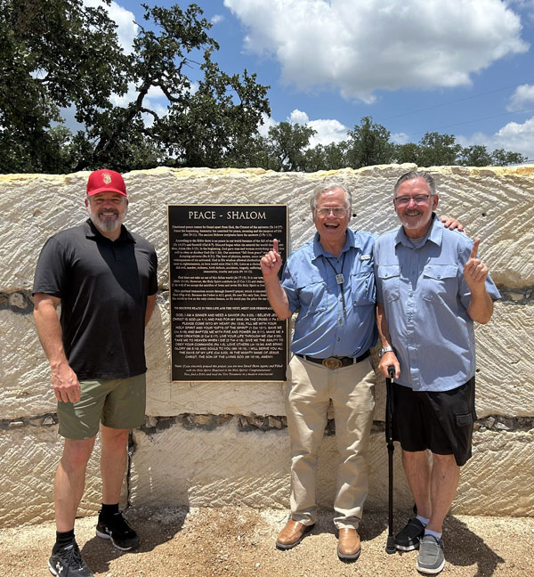 Three men standing in front of unfinished limestone Hill Country Flood Memorial Wall
